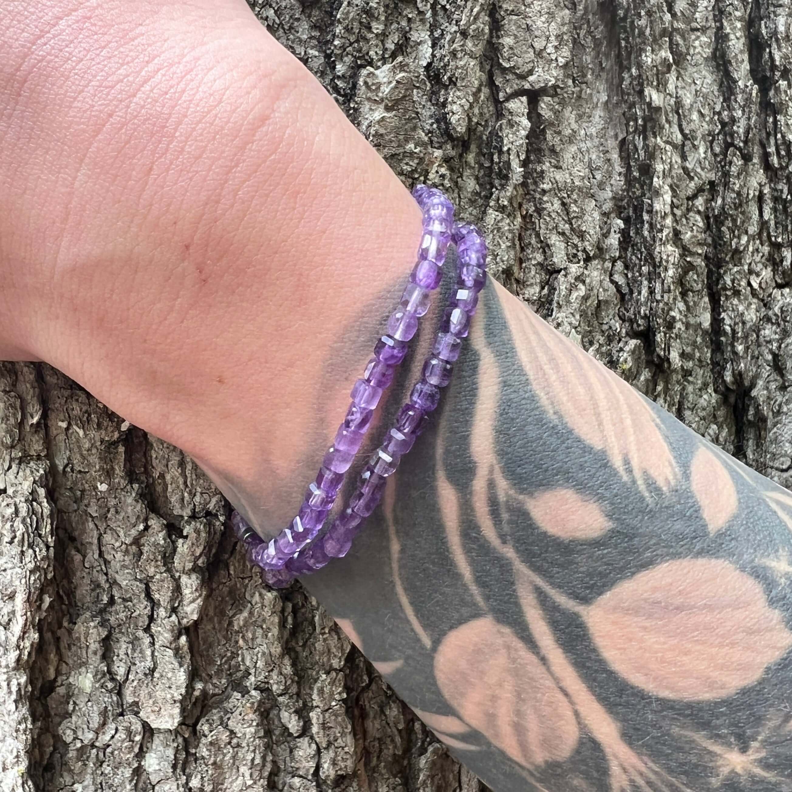 Two amethyst cube bead bracelets on a hand model with tree bark background.