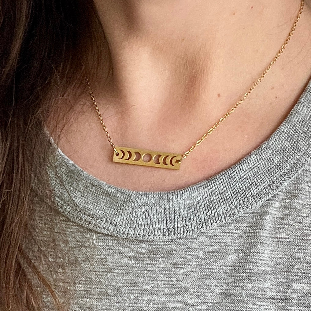 Gold necklace with a bar pendant featuring cut-out circles worn by a person.