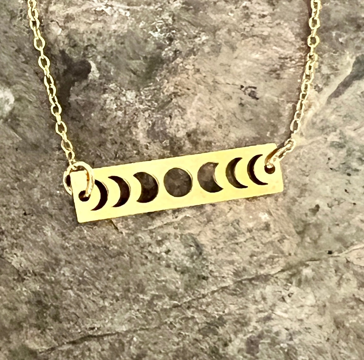Gold necklace with moon phase design on a stone surface