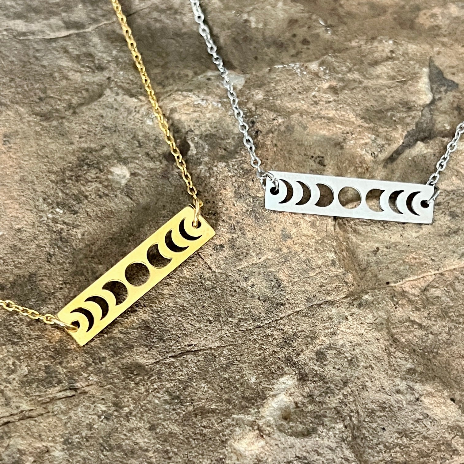 Two necklaces with bar pendants featuring moon phases on a stone surface.