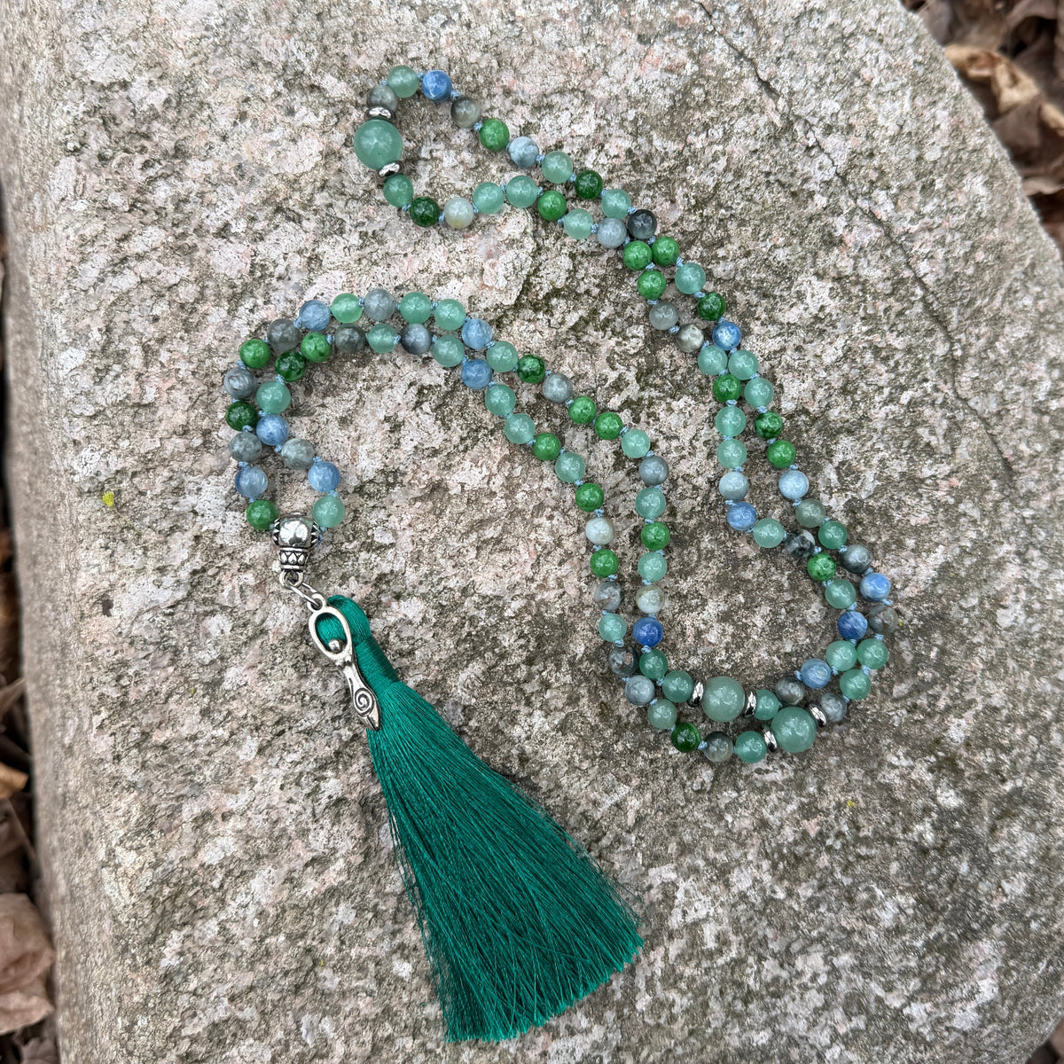 Green beaded necklace with a tassel on a stone surface
