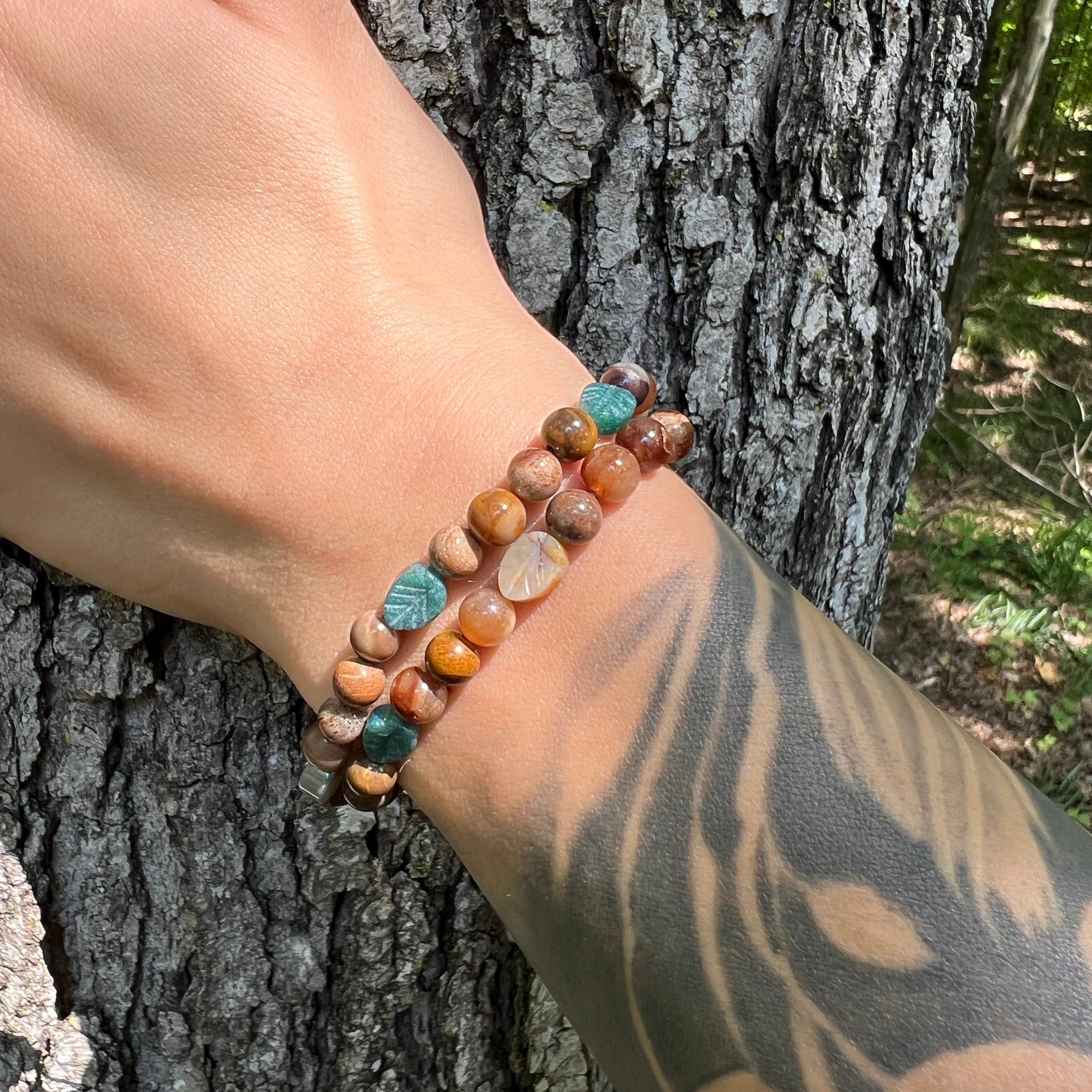 Hand wearing a beaded bracelet against a tree trunk