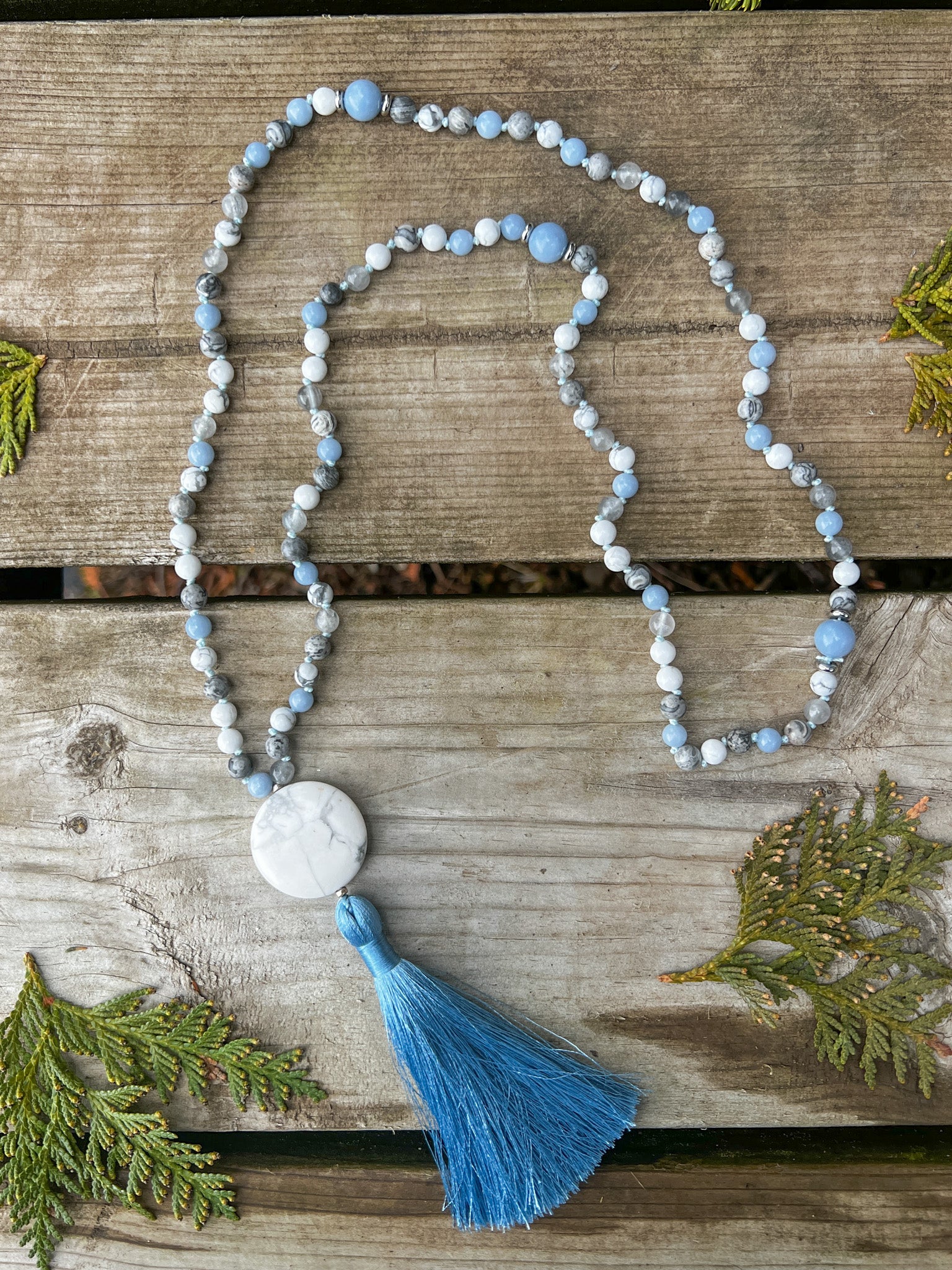 Handmade Open Sky Mala Necklace featuring genuine Howlite, Angelite, and Silver Crazy Lace Agate gemstones arranged on a rustic wooden surface.
