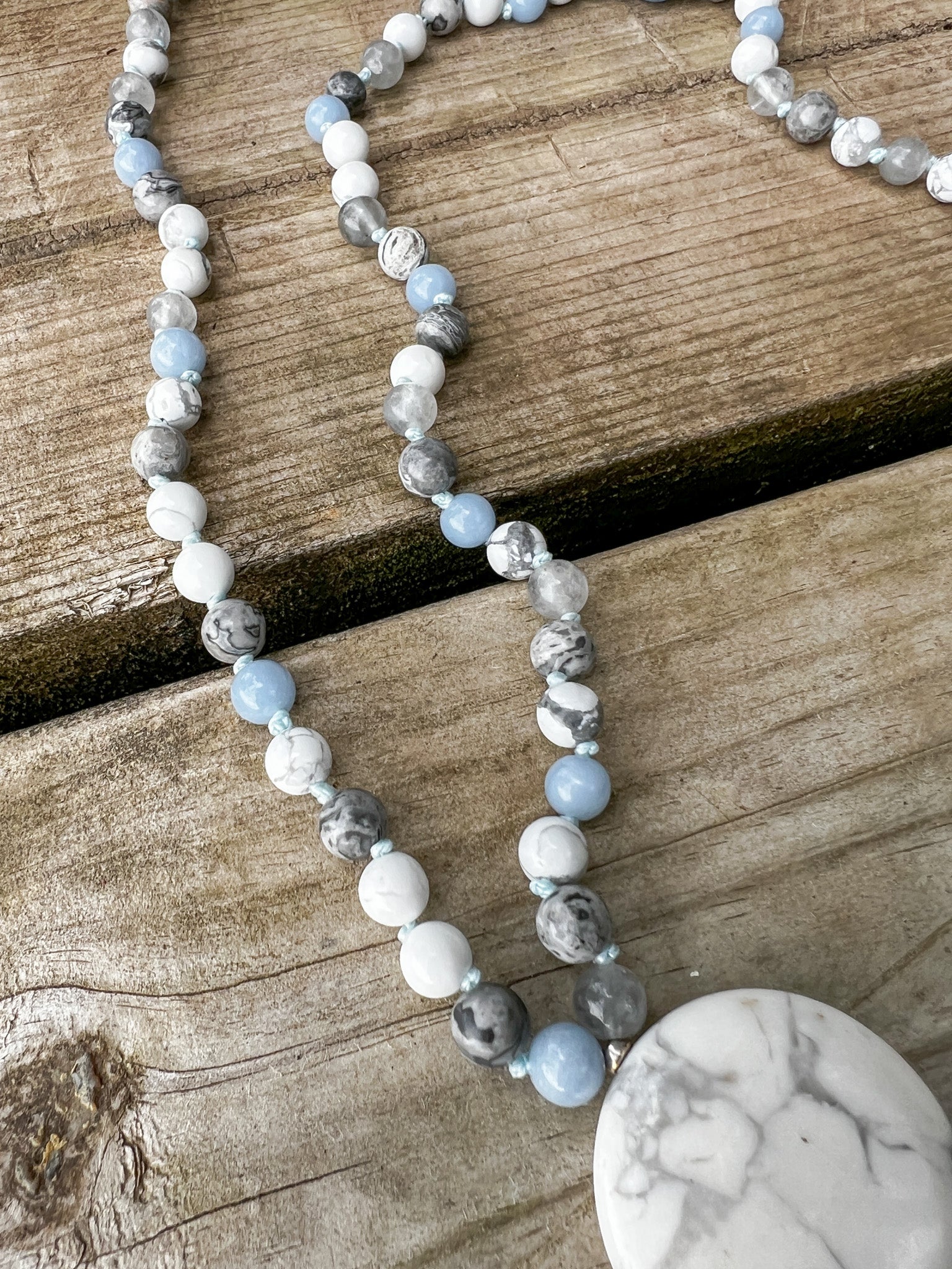 Close-up of the Open Sky Mala Necklace featuring Angelite marker beads, stainless steel accents, and hand-knotted Howlite and Silver Crazy Lace Agate gemstones.