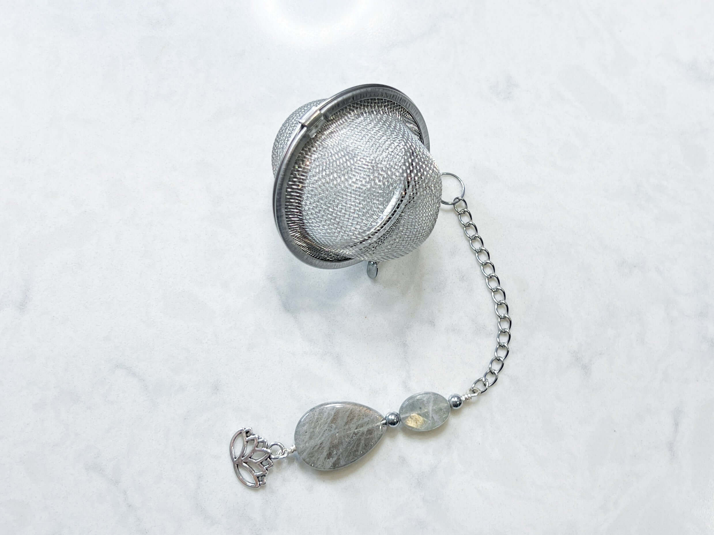 Labradorite Tea Strainer This tea strainer is made with a stainless steel tea ball, Labradorite and Hematite stones with a lotus flower charm. These stones bring the user protection and encourages spiritual transformation.