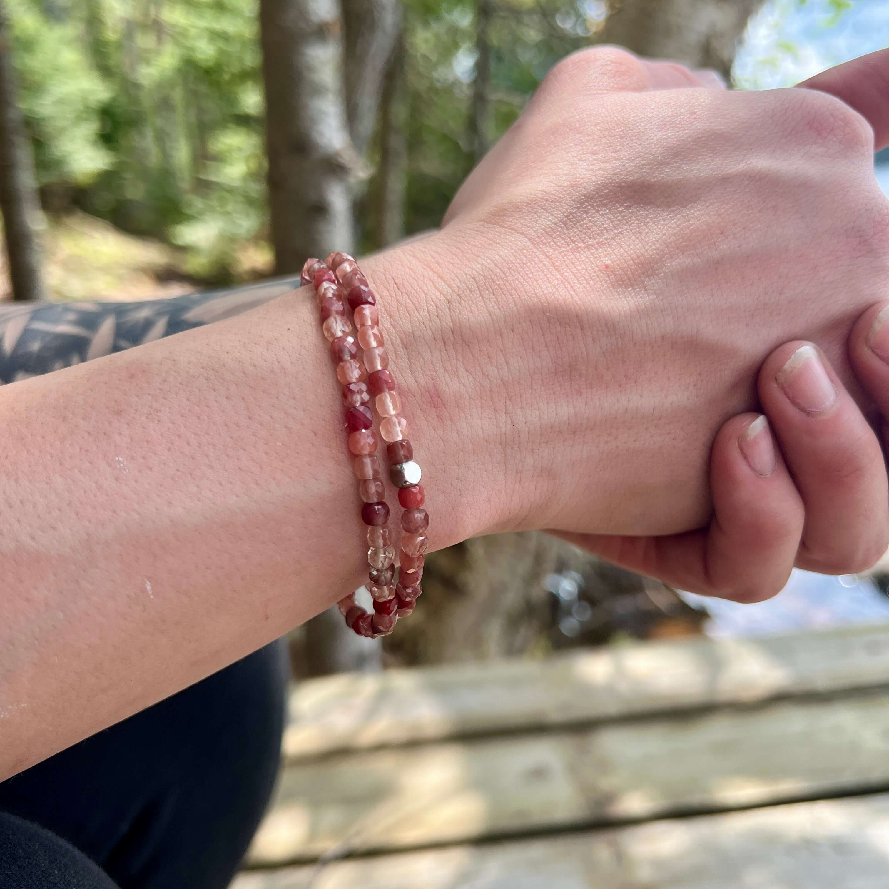 Two Red Lazasine bracelets on hand model.