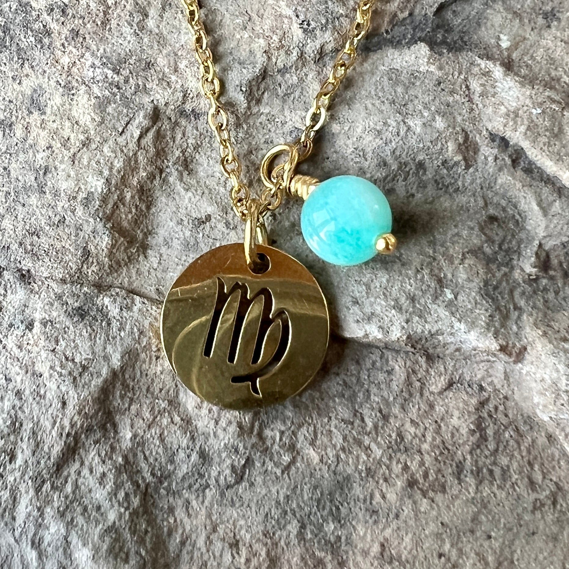 Gold necklace with a Virgo symbol pendant and amazonite bead on a stone surface