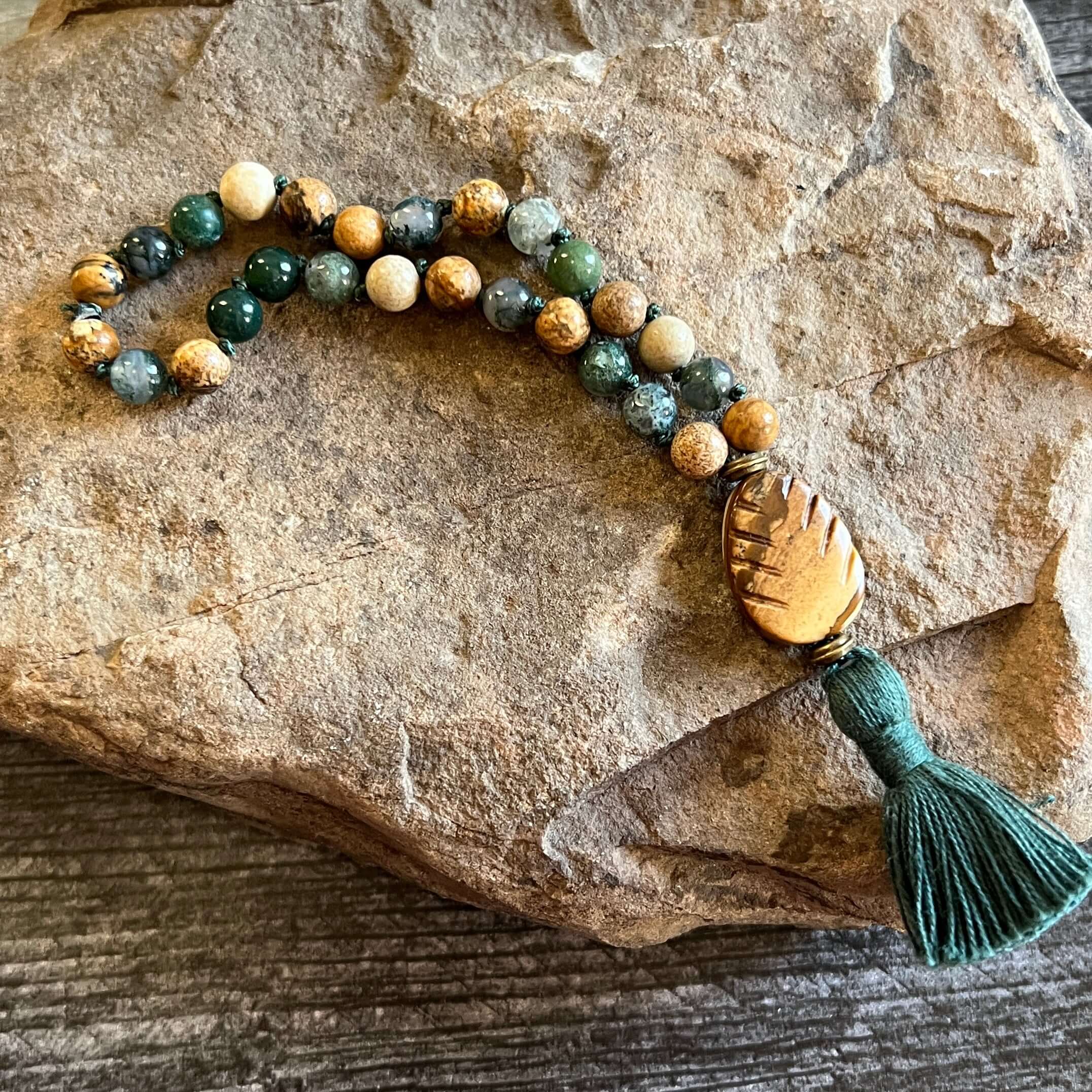 Pine Tree Quarter Mala This quarter mala is made with high-quality Picture Jasper and Moss Agate gemstones which bring confidence and abundance to the wearer. Zodiac Signs: Leo, Capricorn, & Virgo. Chakras: Root, Third Eye, & Heart. Handmade with authenti