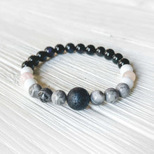 Load image into Gallery viewer, Lava Stone Focal Bracelet with Rainbow Obsidian This bracelet is made with a Lava stone focal bead, Gray Map Jasper, White Jade, Pink Morganite, and Rainbow Obsidian. Together these stones bring the wearer a sense of relaxation, and a release of stagnant
