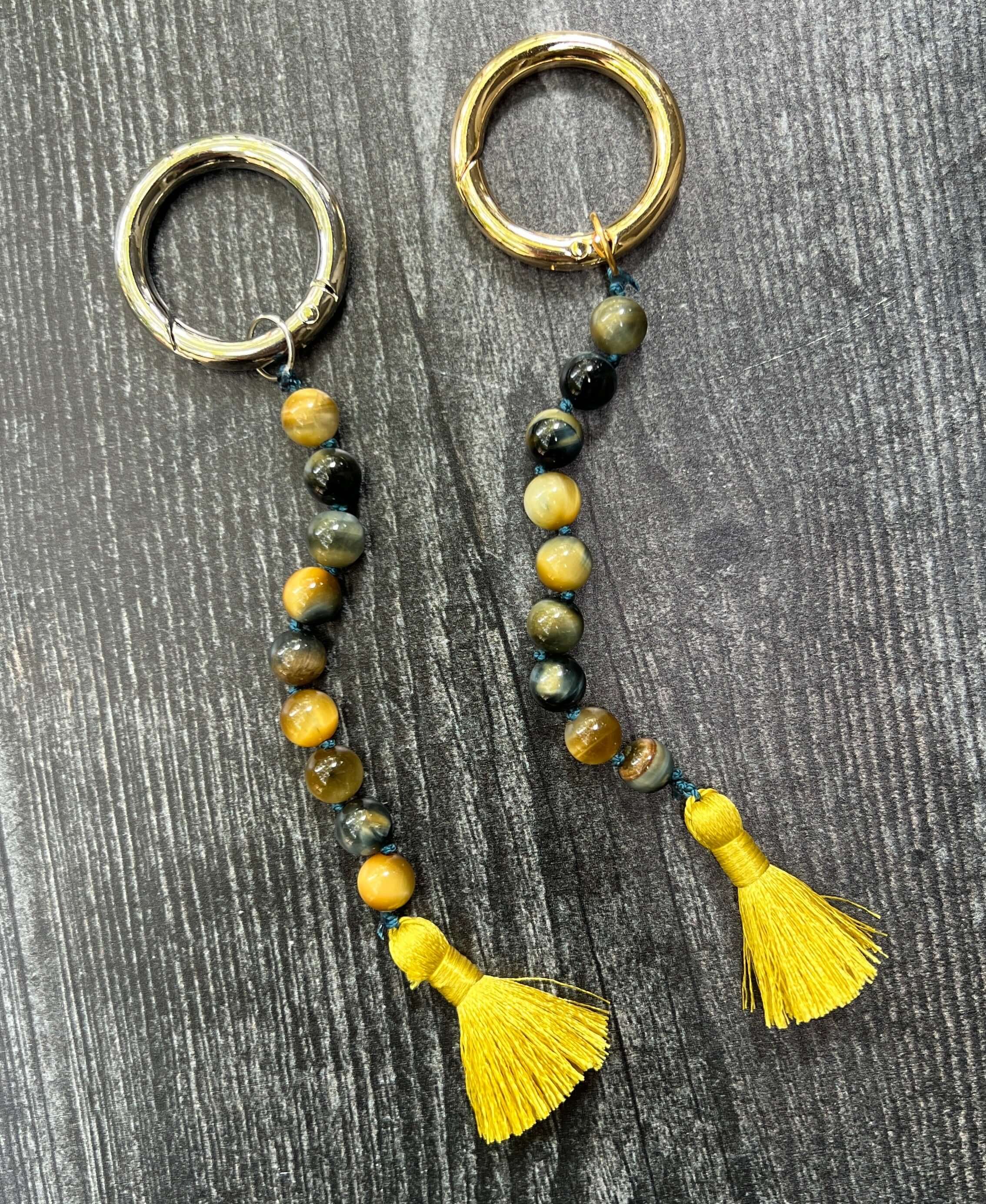 Two keychains with beaded chains and yellow tassels on a wooden surface