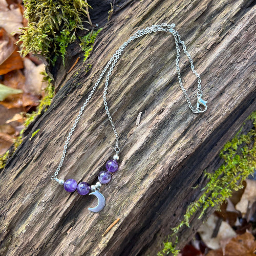 Amethyst Moon Necklace This beaded necklace is made with Amethyst which brings the wearer a sense of calmness and clarity. Amethyst is the birthstone for the month of February. A stainless steel crescent moon finishes off the piece.