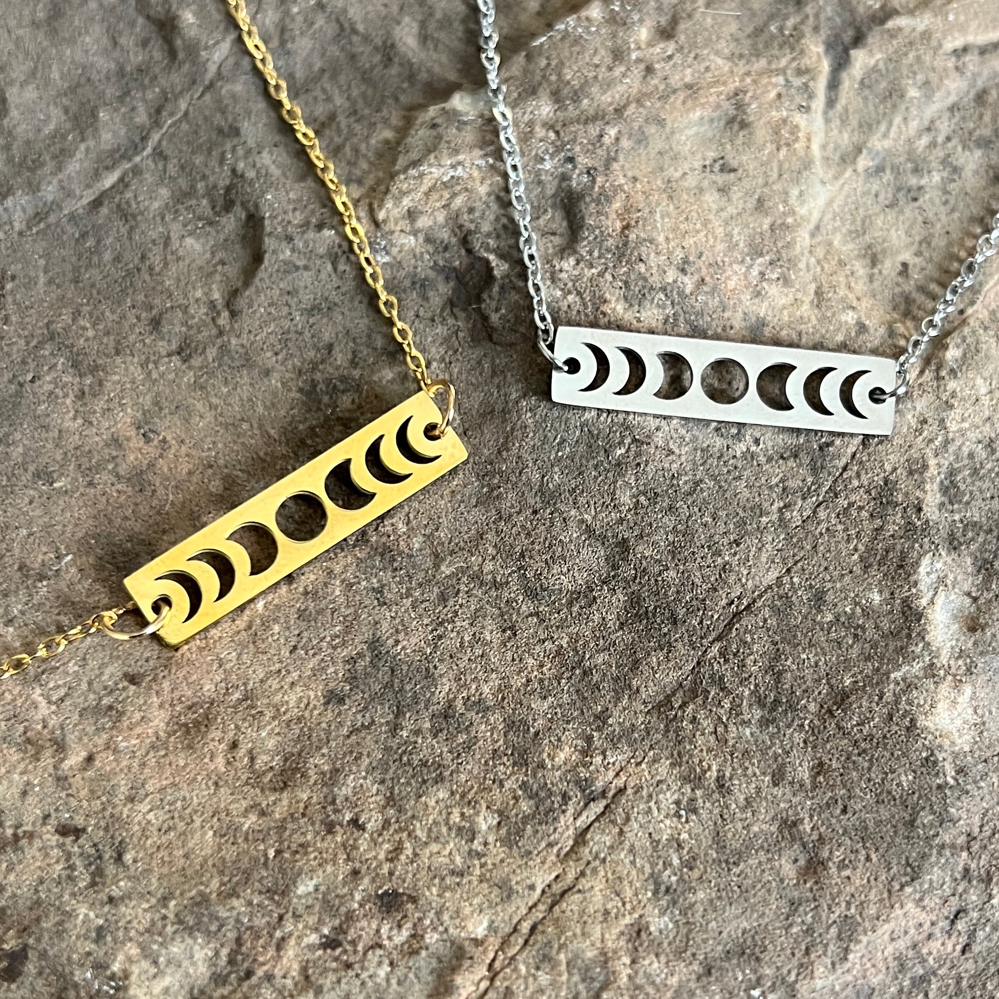 Two bar necklaces with moon phase designs on a stone surface