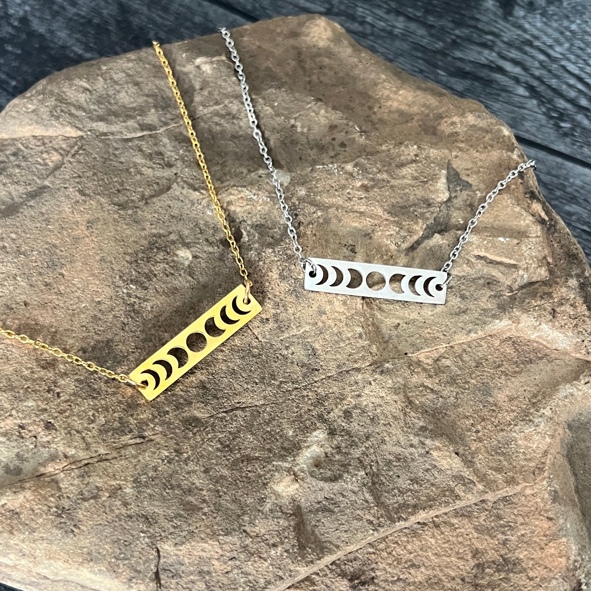 Two necklaces with moon phase designs on a stone surface