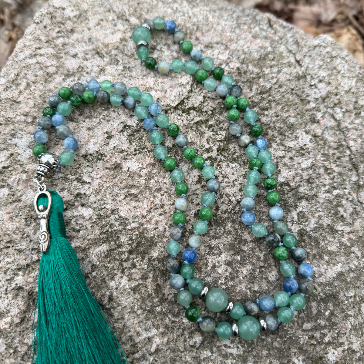 Green beaded necklace with a tassel on a textured stone surface