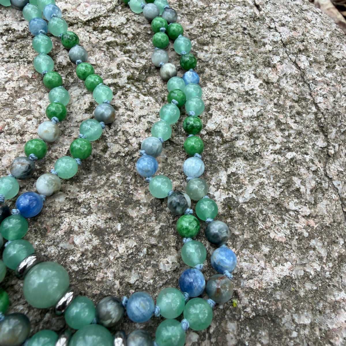 Green and blue beaded necklace on a textured stone surface