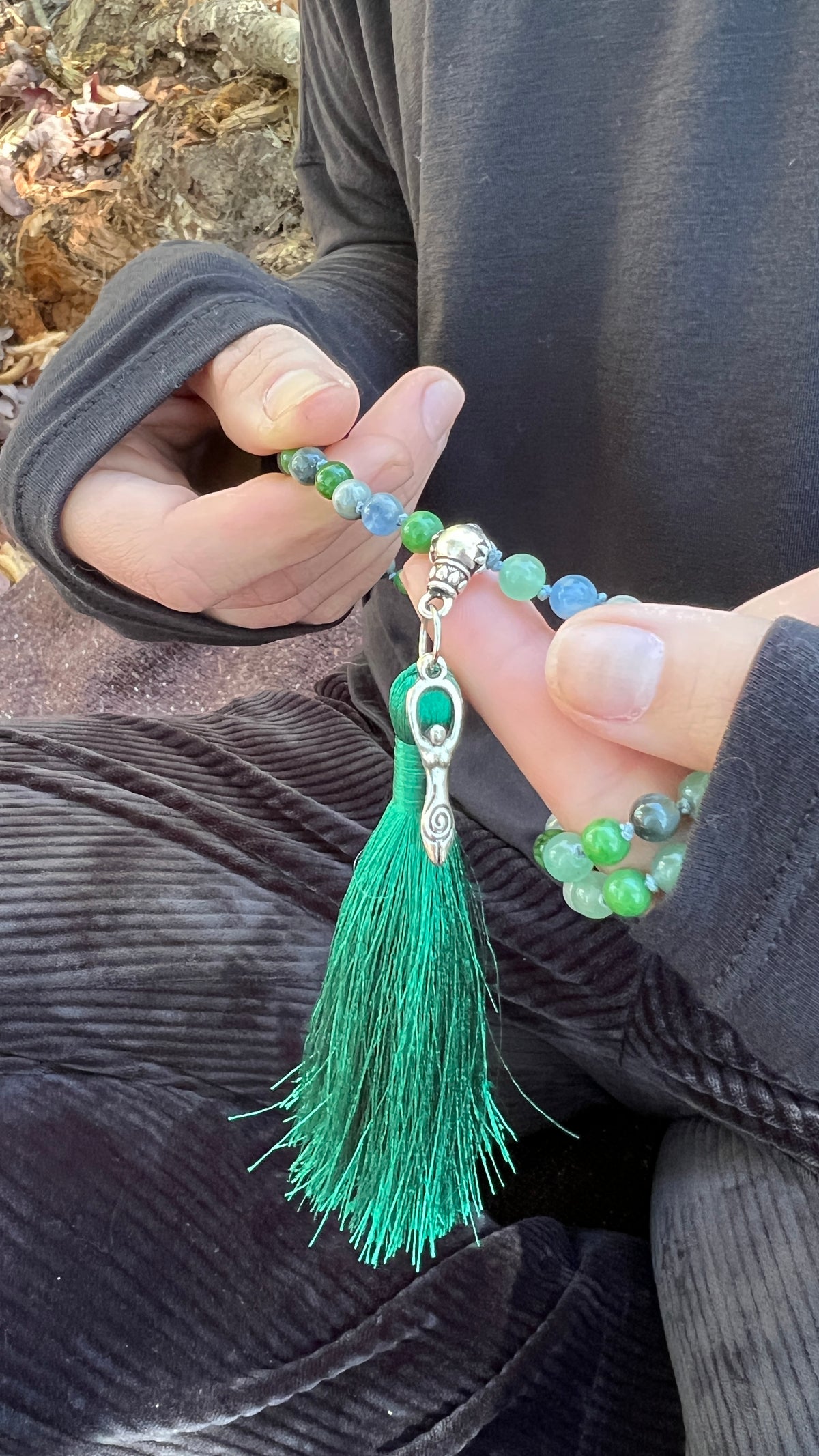 Person holding a green beaded bracelet with a tassel