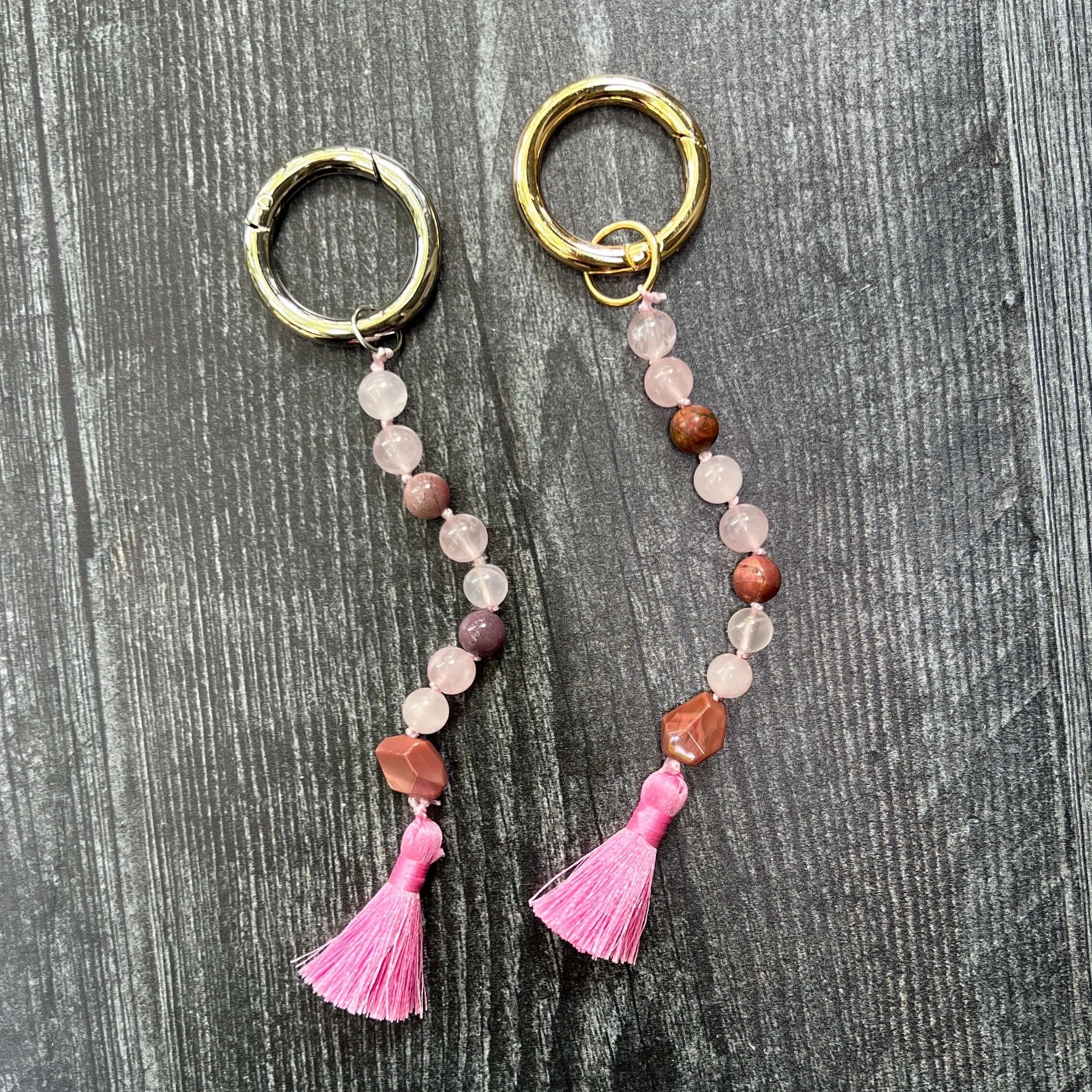 Pair of keychains with pink tassels and beaded chains on a wooden surface