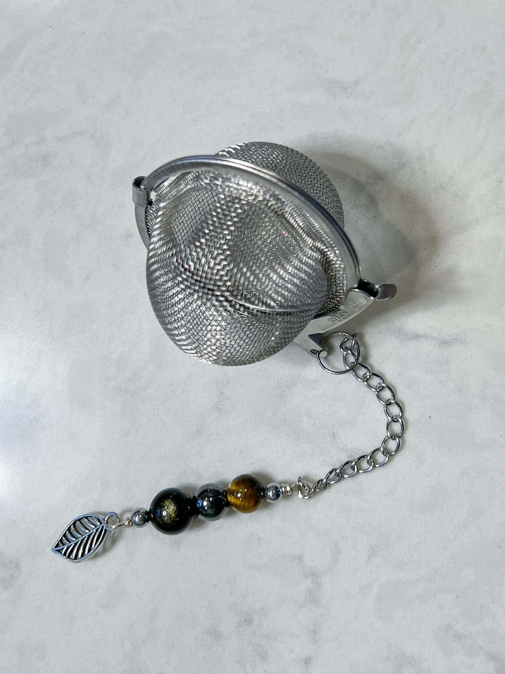 Triple Protection Tea Strainer This tea strainer is made with a stainless steel tea ball and gold sheen obsidian, hematite, and tiger eye. These stones offer protection against negative energy of all kinds- inner, spiritual, and environmental.