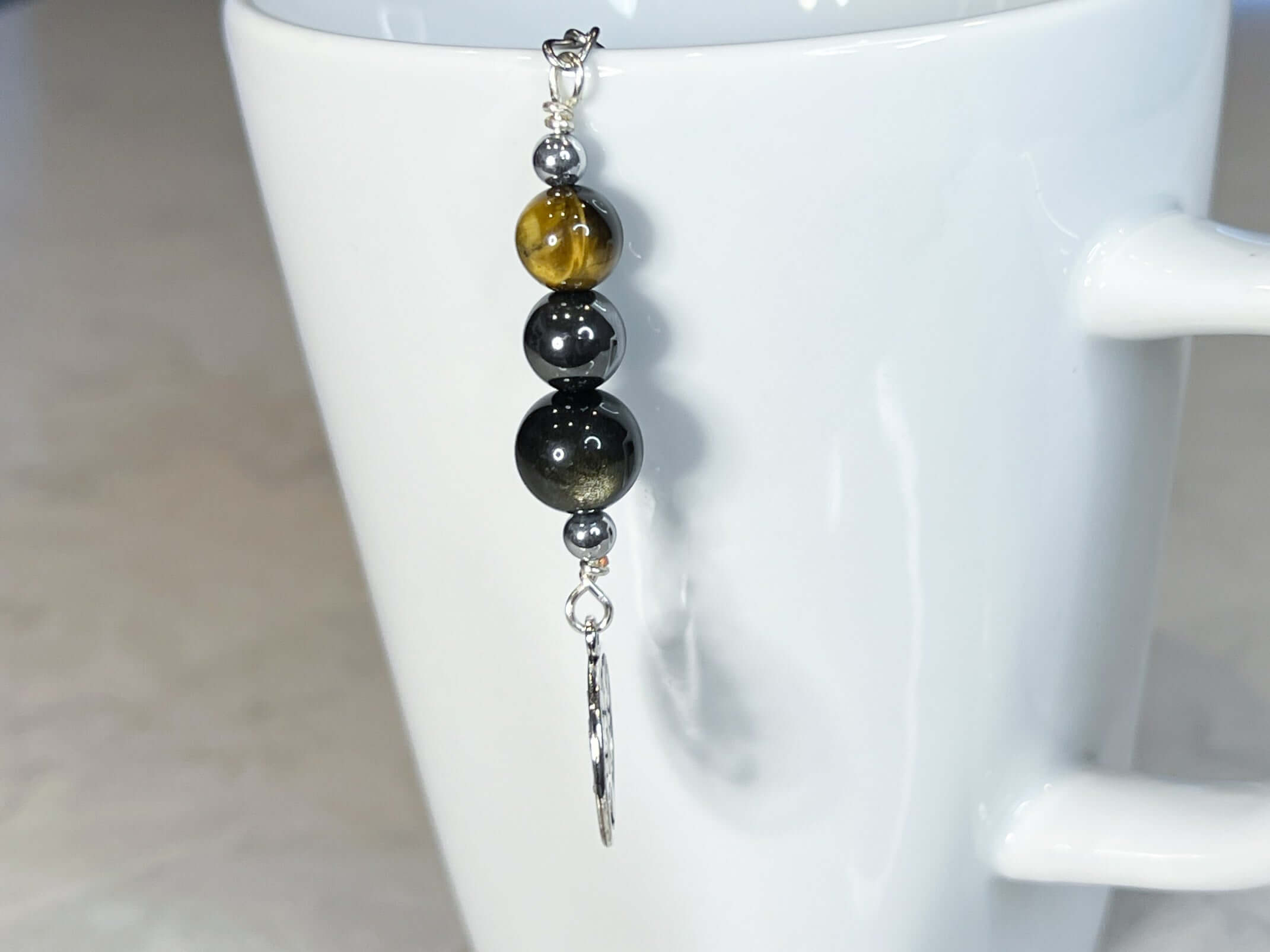 Triple Protection Tea Strainer This tea strainer is made with a stainless steel tea ball and gold sheen obsidian, hematite, and tiger eye. These stones offer protection against negative energy of all kinds- inner, spiritual, and environmental.