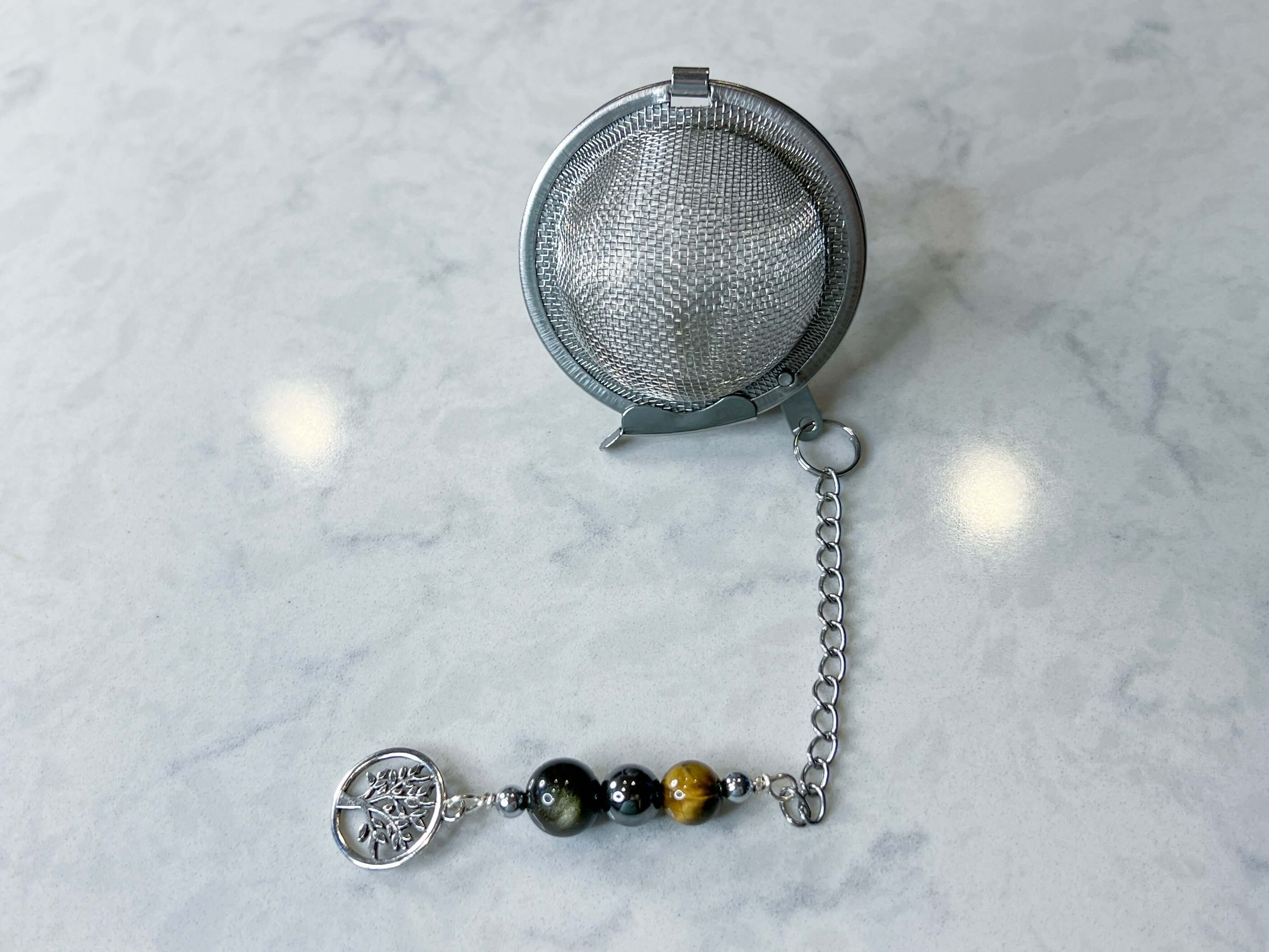 Triple Protection Tea Strainer This tea strainer is made with a stainless steel tea ball and gold sheen obsidian, hematite, and tiger eye. These stones offer protection against negative energy of all kinds- inner, spiritual, and environmental.