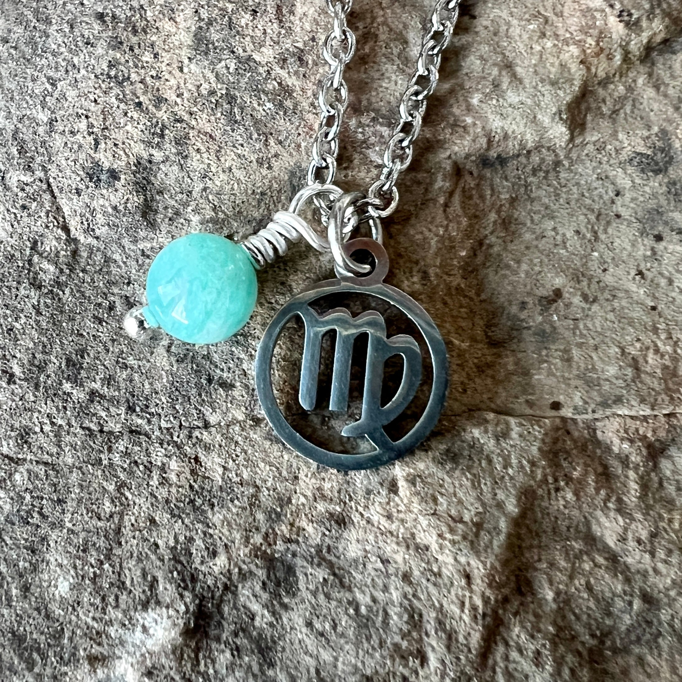 Necklace with a amazonite bead and Scorpio symbol stainless steel charm on a stone background
