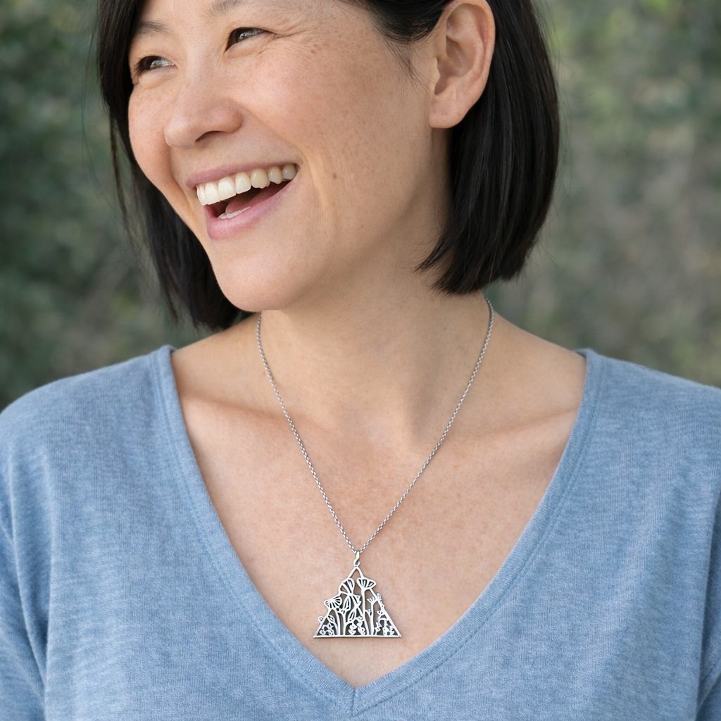 Woman wearing a silver necklace with a tree pendant against a blurred natural background